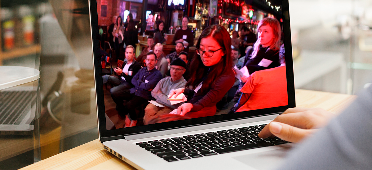 A laptop shows a photo of a Cycle Toronto member casting their vote at the 2019 Cycle Toronto Annual General Meeting. In the background, a group of people look on.