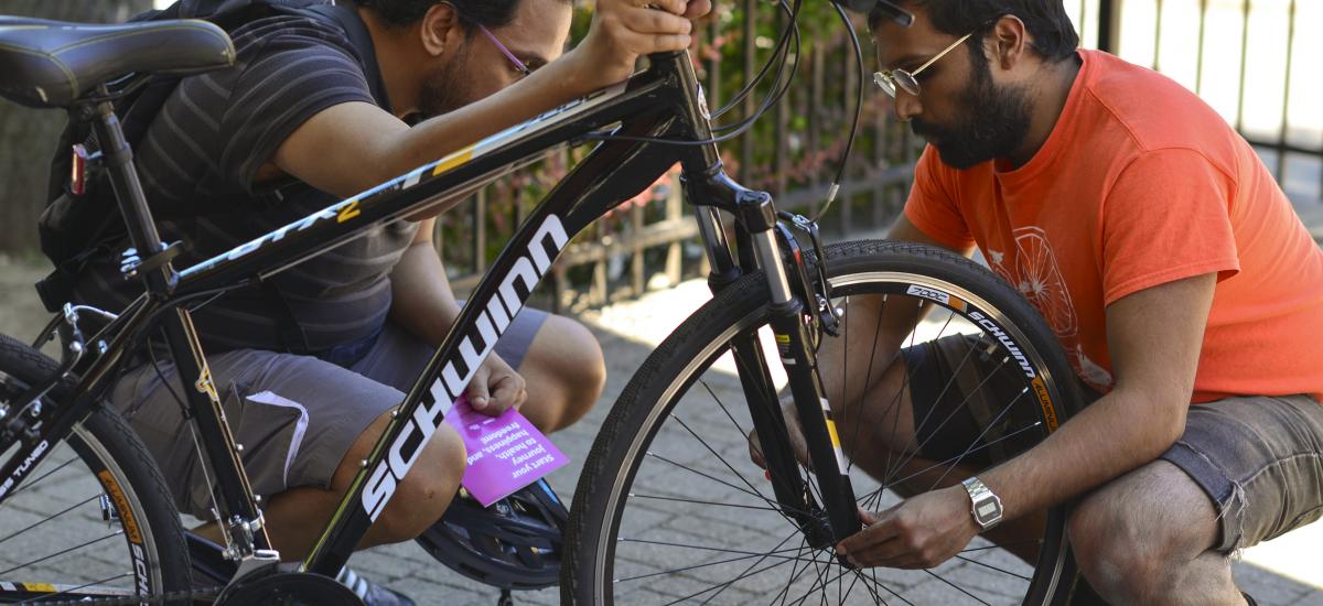 A man examines a bike wheel while his student looks on.