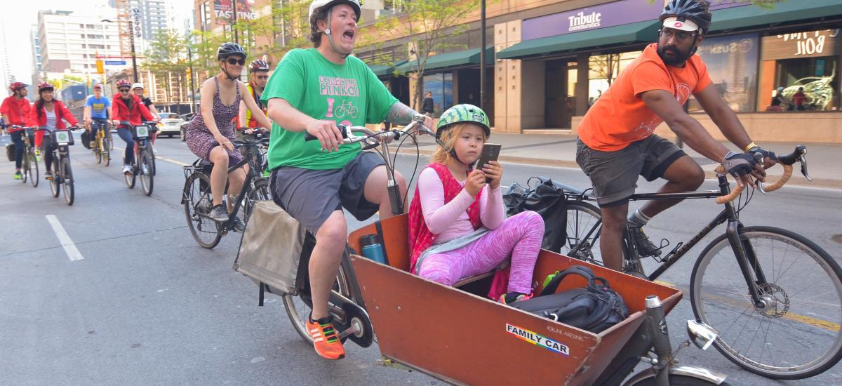 Person rides a cargo bike with a child in the front while others ride bikes nearby.