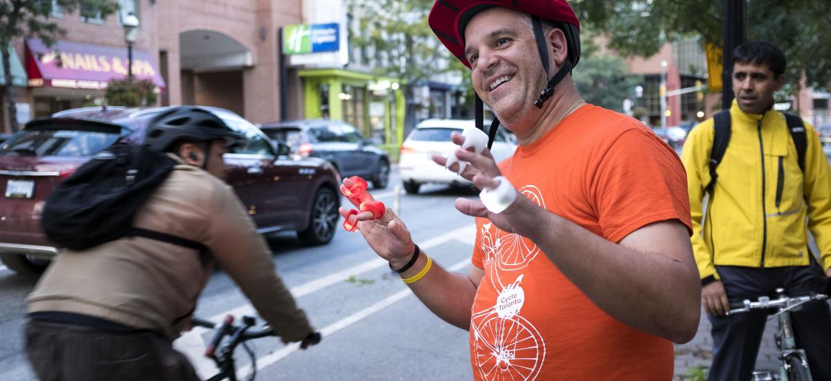 Smiling person in orange shirt hands out bike lights to passing cyclists