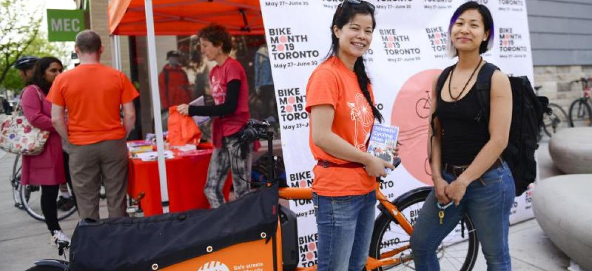 Two people stand in front of a orange Cycle Toronto tent smiling.