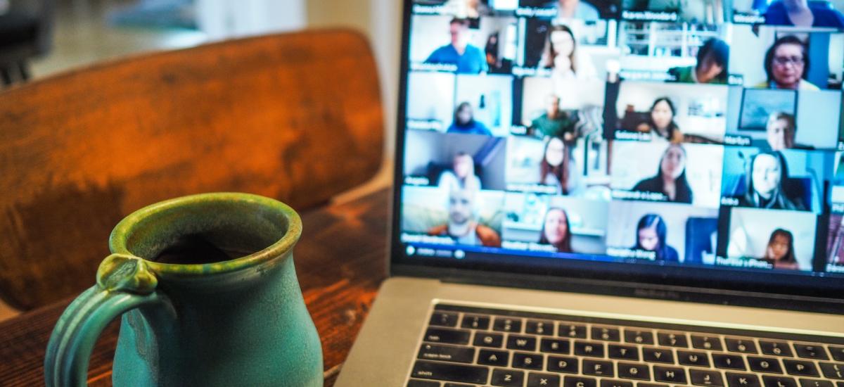 Photo of a laptop and coffee mug sitting on a table. A video call is shown on the laptop, but the faces of the participants are blurry.