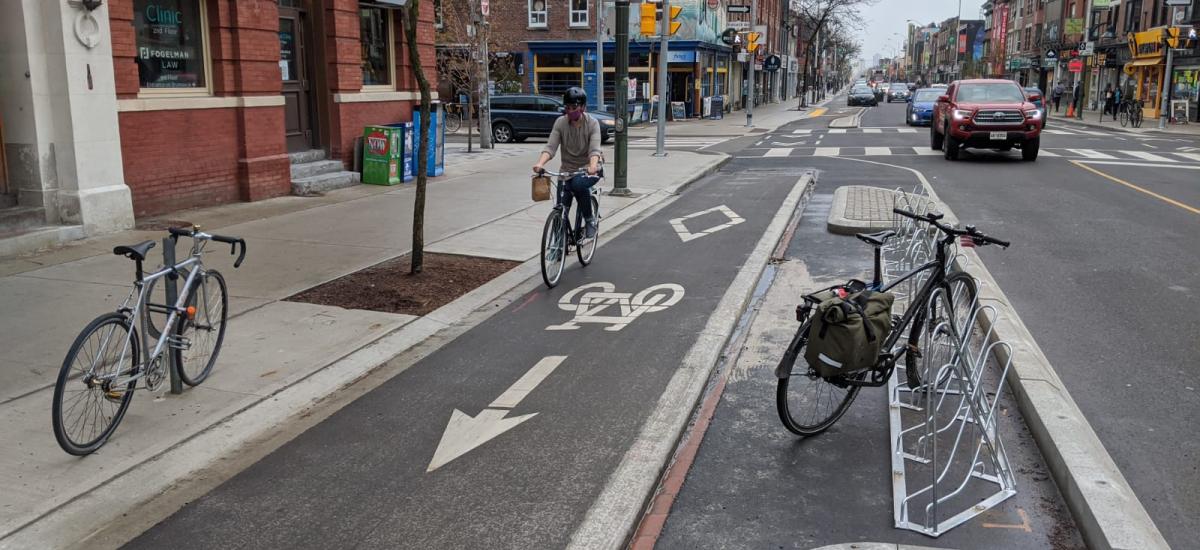 Person rides a bike in a raised bike lane beside a bike rack