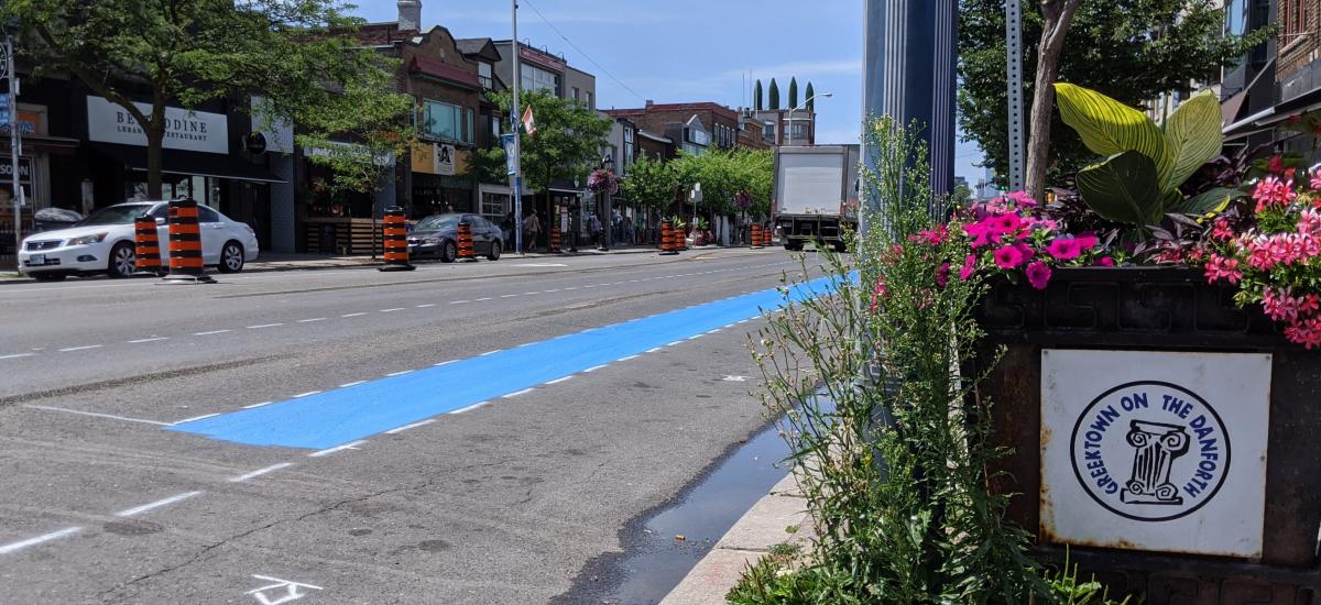 A swath of blue paint runs through a construction zone. A sign reads "Greektown on the Danforth"