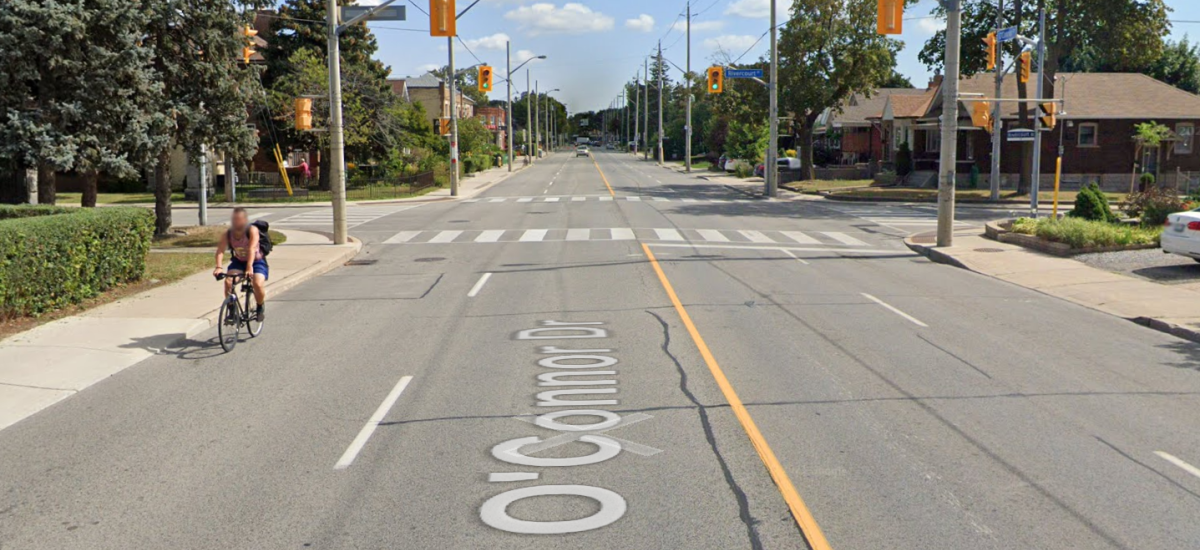 A person rides a bike on a wide road lined by houses