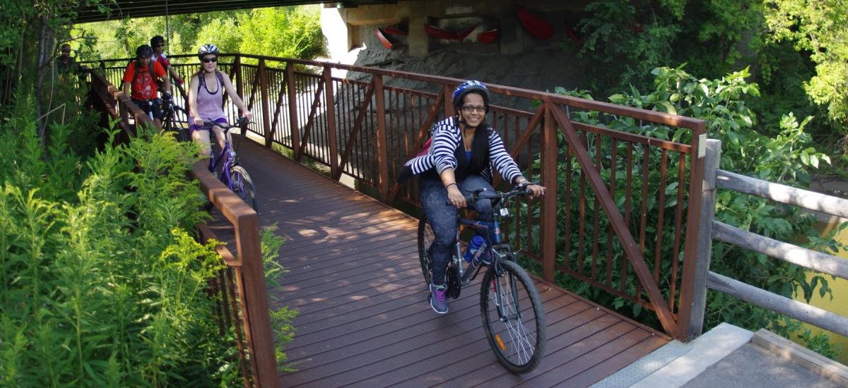 Smiling people ride bikes over a bridge.