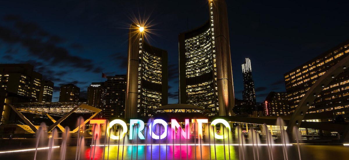 Multi-couloured Toronto sign at night with a water fountain in front of it