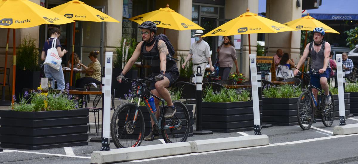 A person rides a bike past people dining streetside