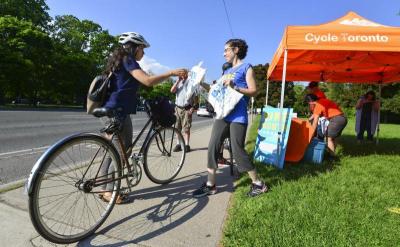 A smiling person hands a reusable bag filled with goodies to a person on a bike.