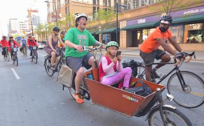 Person rides a cargo bike with a child in the front while others ride bikes nearby.