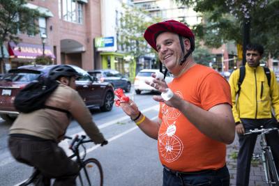 Smiling person in orange shirt hands out bike lights to passing cyclists