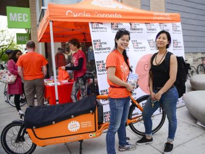 Two people stand in front of a orange Cycle Toronto tent smiling.