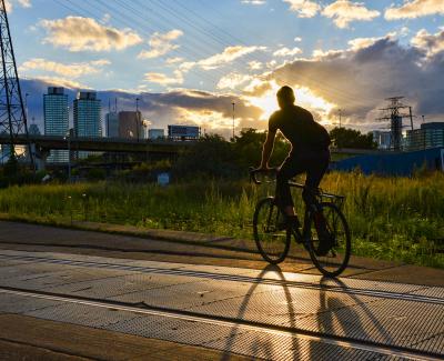 A person rides a bike over streetcar tracks in an industrial area. The setting sun outlines them leaving their shape a shadow in the foreground.