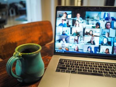 Photo of a laptop and coffee mug sitting on a table. A video call is shown on the laptop, but the faces of the participants are blurry.