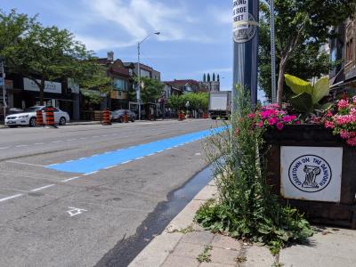 A swath of blue paint runs through a construction zone. A sign reads "Greektown on the Danforth"