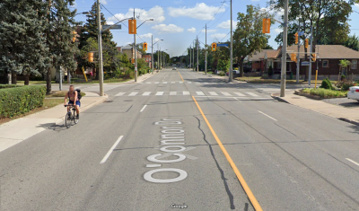 A person rides a bike on a wide road lined by houses