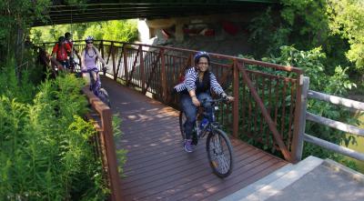 Smiling people ride bikes over a bridge.