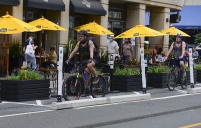 A person rides a bike past people dining streetside