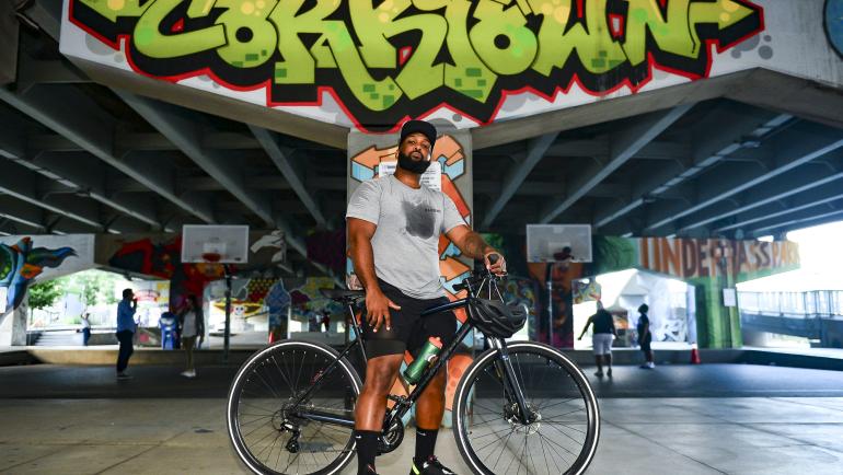 Christopher McGarrell poses with his bike in front of graffiti that says "Corktown"