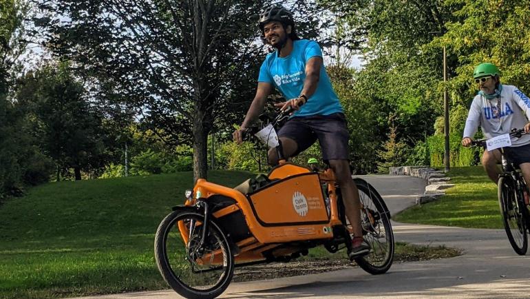 Kevin rides an orange Cycle Toronto cargo bike on a trail in Scarborough