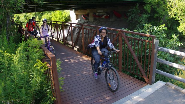 Smiling people ride bikes over a bridge.