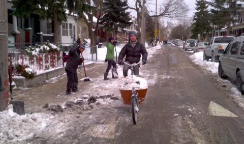 Residents and a person on a bike clearing and removing snow from bike lane 