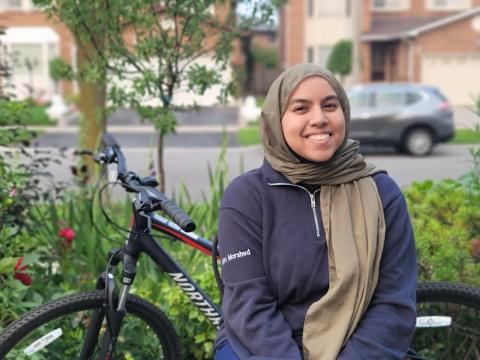 A smiling woman wearing a hijab beside her bike