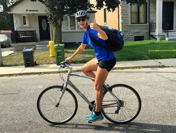 A person on a bike in a blue shirt smiles broadly and gives a thumbs up