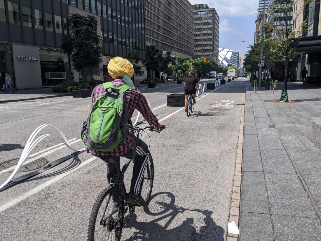 Wavy plastic barriers and empty planters separate a bike lane from traffic. People ride bikes