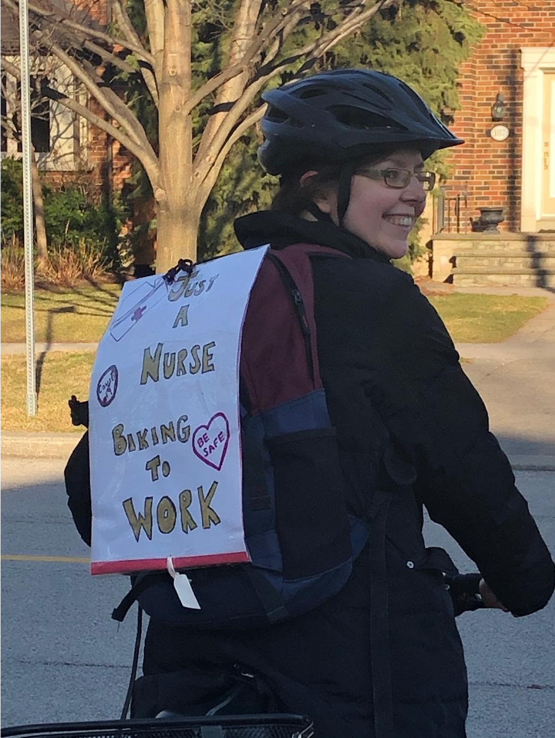 Smiling person on bike wears a sign that says "Just a nurse biking to work"