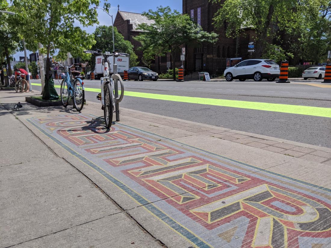 A swath of green paint runs through a road. Parked bikes line the street. A sidewalk mural reads "Together"