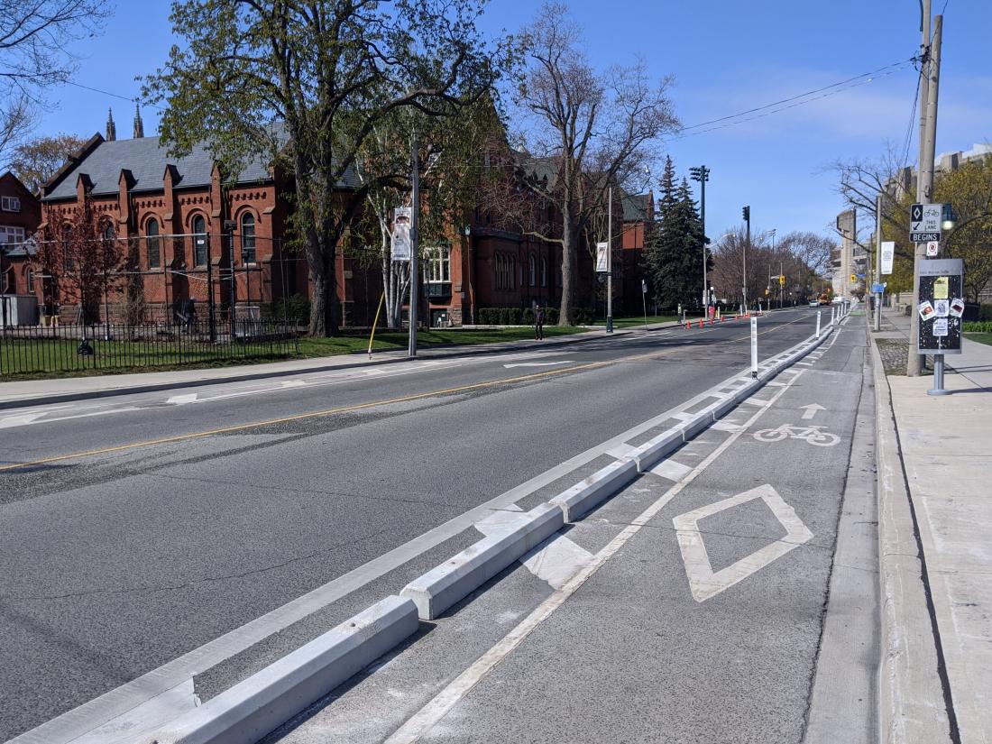 Concrete curbs with occasional plastic posts separate a bike lane from a car lane