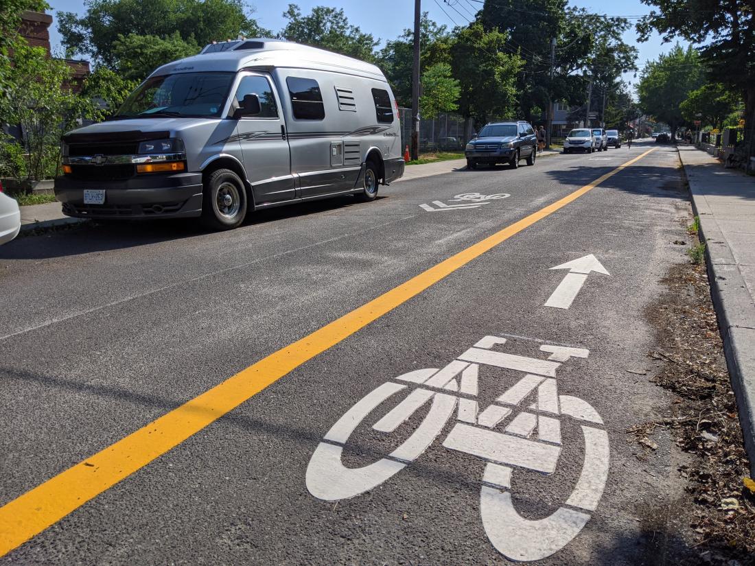 A bike symbol with an arrow is on the right side of the road. A yellow line separates it from oncoming traffic