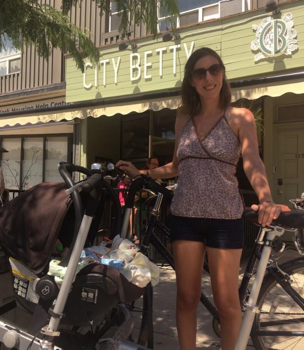 A woman stands beside a combination bike stroller.