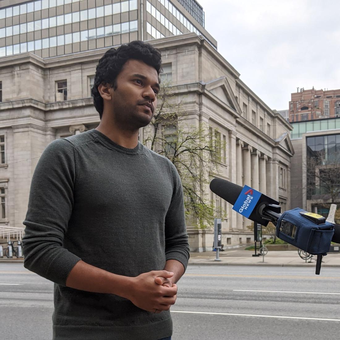 Kevin stands in front of a Global News microphone on a busy street