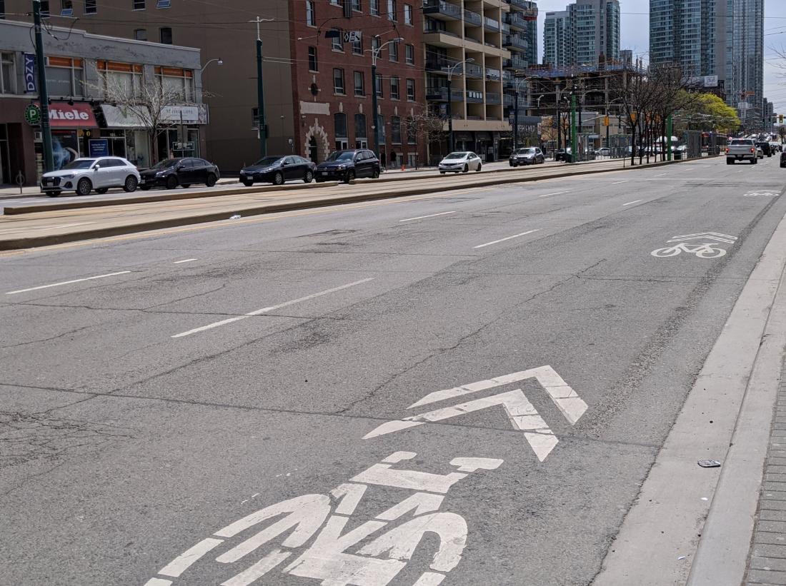 A wide road has bike symbols with chevrons above them on the right side