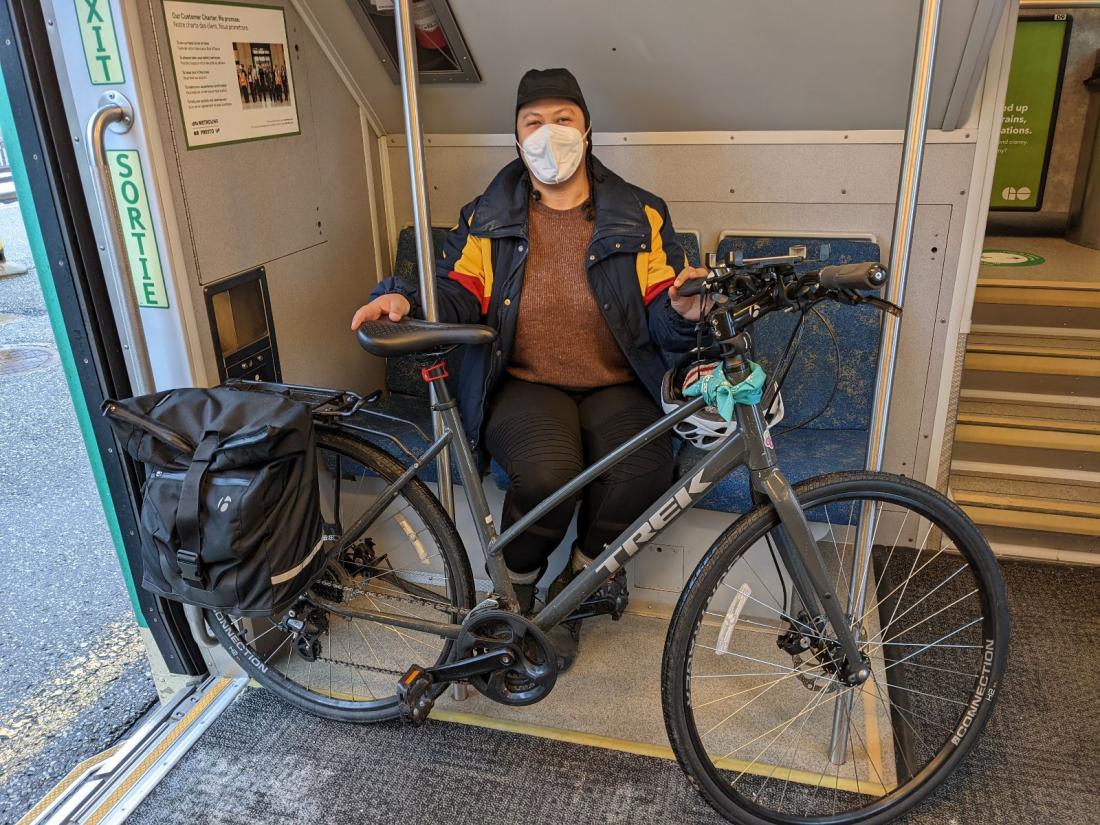 Taneisha sits inside a GO train with her bike while wearing a mask