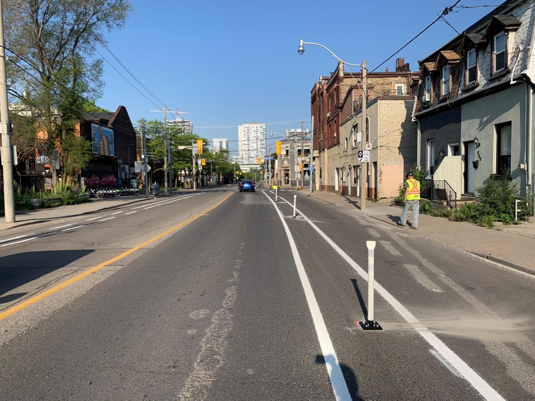 Streetcar tracks run down the middle of a street. The outside lanes have bollard separated bike lanes